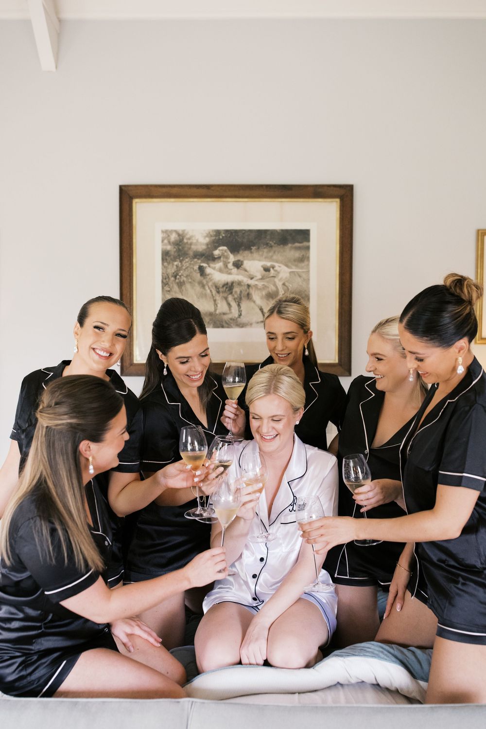 Group wearing matching satin sleepwear while celebrating with champagne glasses in a bedroom setting.