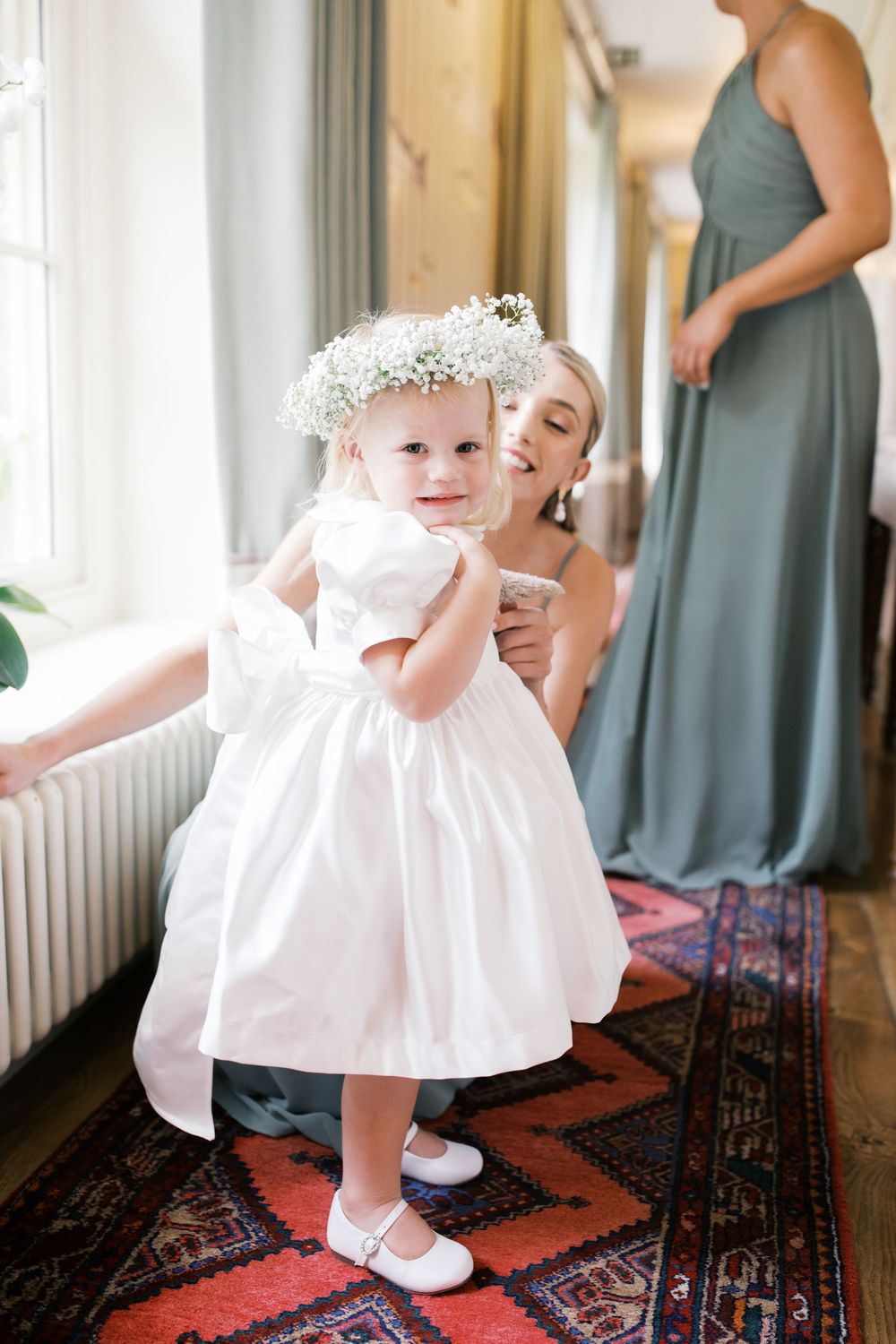 Little one in white dress with floral crown twirls playfully in sequence of photos on vintage oriental rug.