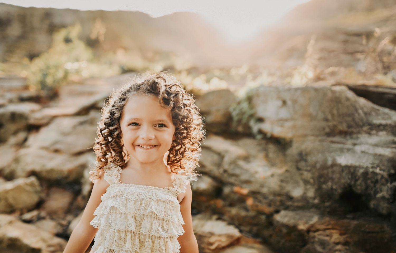 a curly haired little girl in a boho lace dress smiles as she plays on the rocks at murrell park