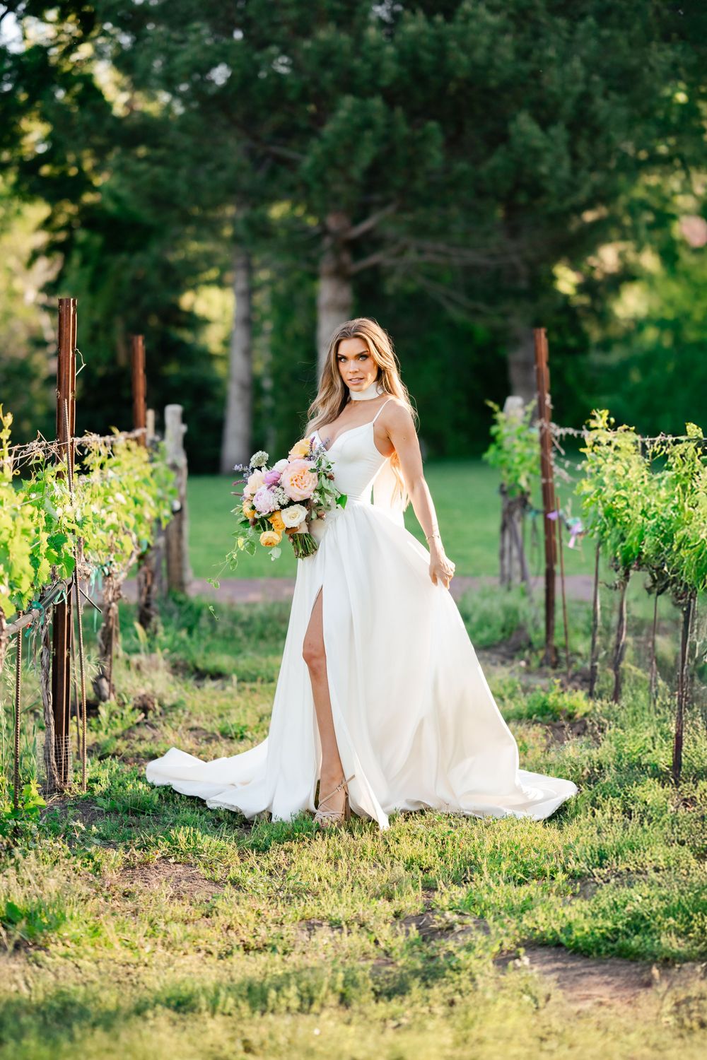 Beautiful white wedding dress with high slit photographed in romantic vineyard setting at golden hour.