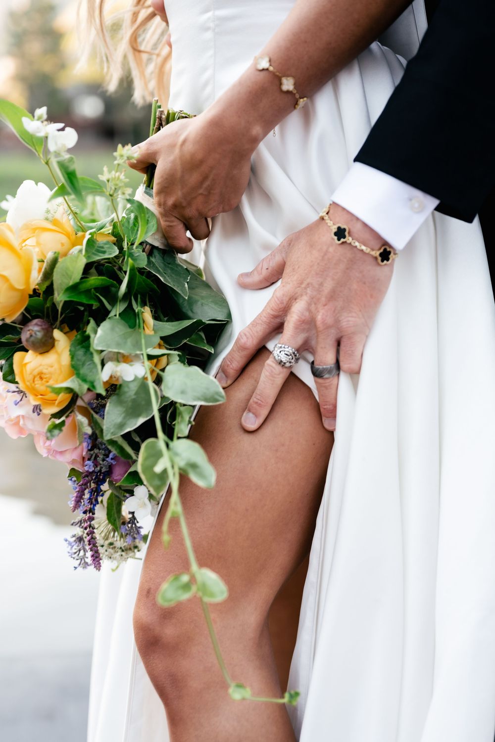A bride in white showing her garter with yellow flower bouquet against neutral background.
