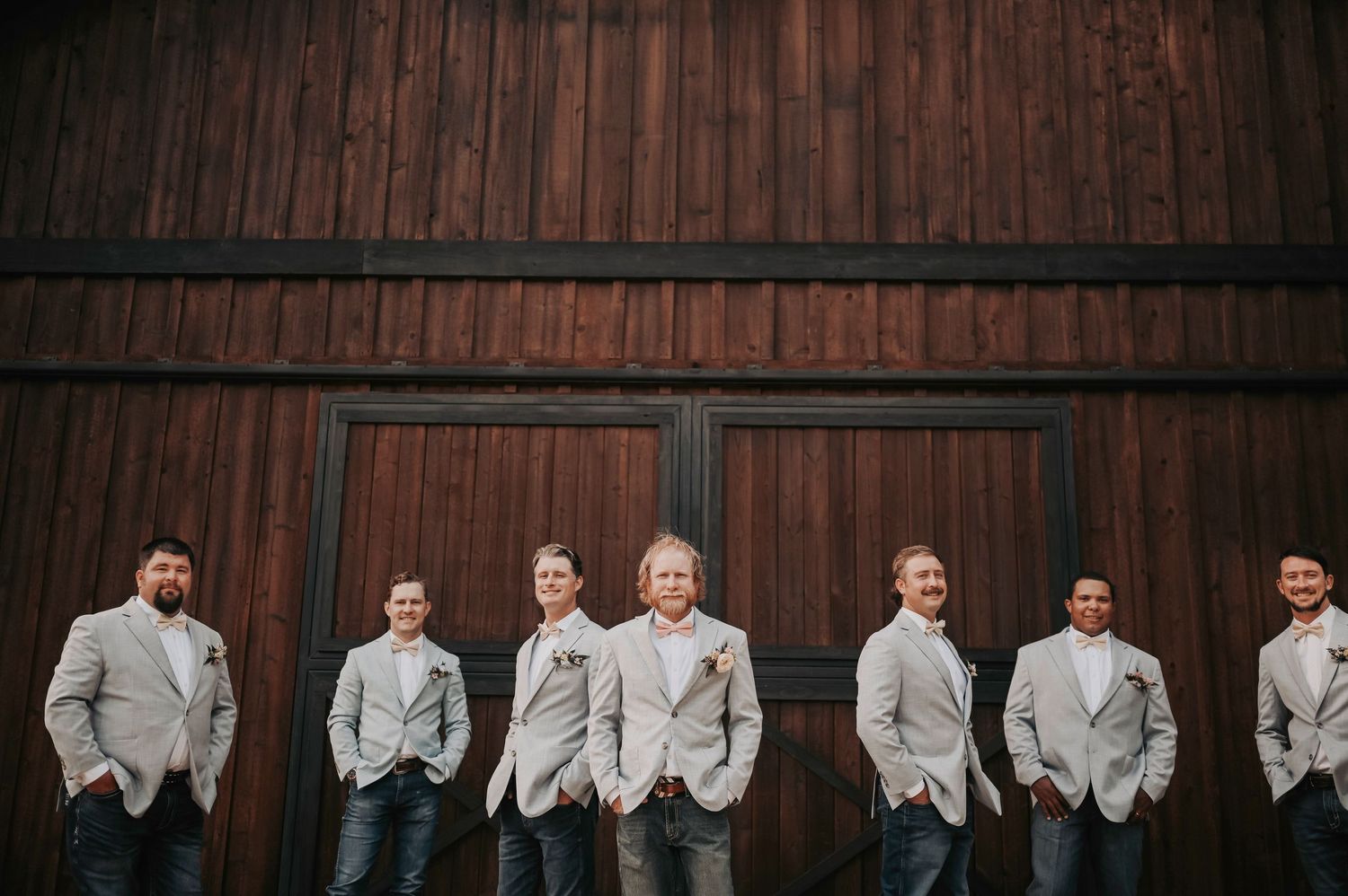 Groom and groomsmen striking cool poses in front of a rustic barn