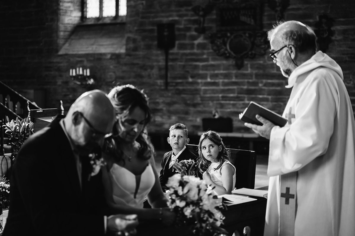 Vigselakt i Klosterkyrkan i Vadstena, brudparet står på knä framför altaringen där prästen står, fokus är på de små brudnäbbarna.
