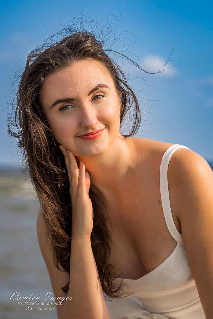 Portrait capture against blue sky and water showing windswept dark hair and natural lighting.