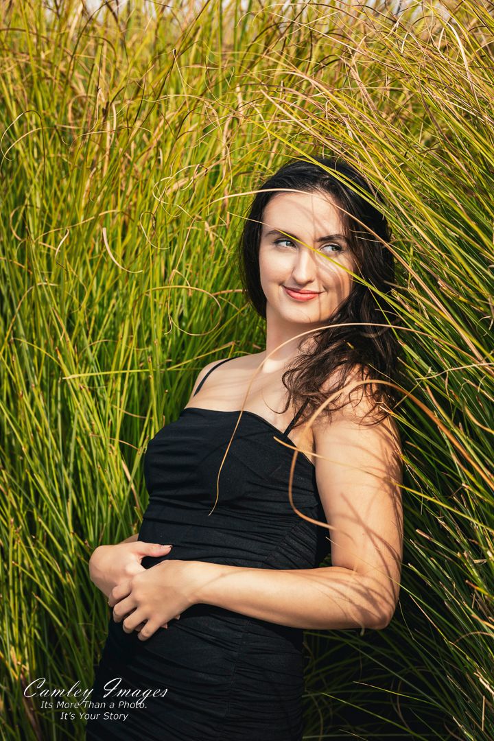Woman in black dress poses in front of tall ornamental grass during golden hour.