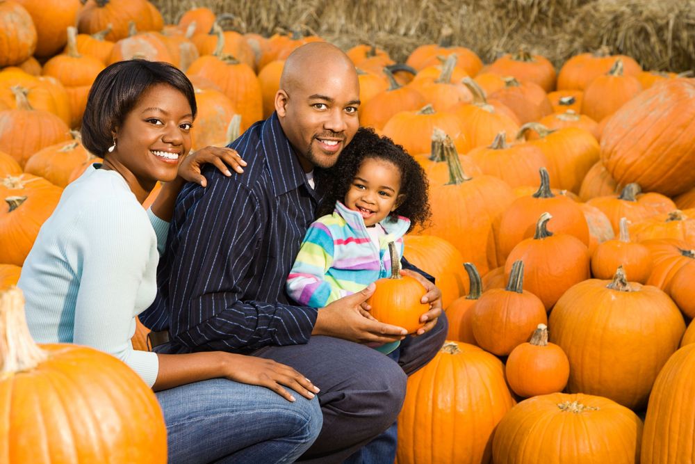 Family sitting together among bright orange pumpkins at autumn pumpkin patch.