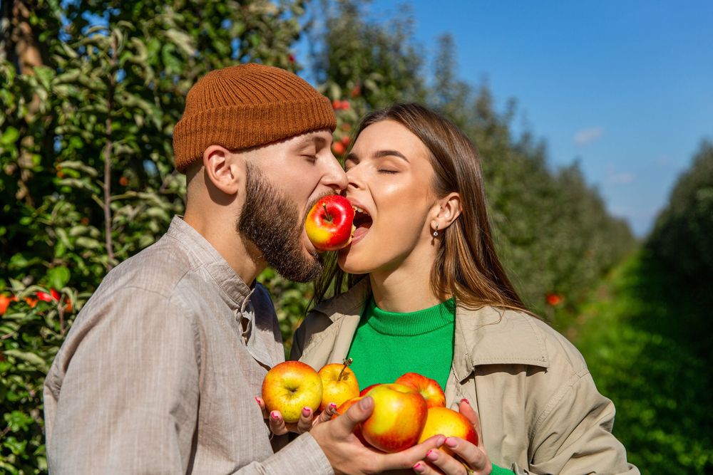 Two people hold fresh citrus fruits in a sunny garden while sharing an intimate moment together.
