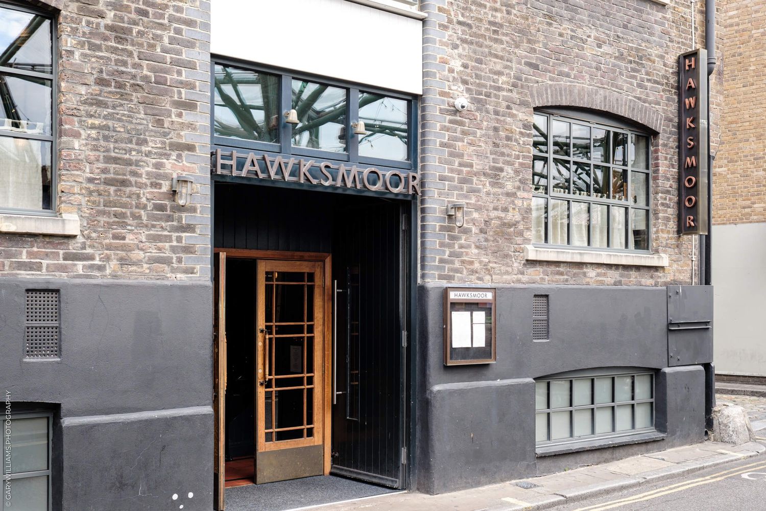 Modern gray and brick facade of a restaurant entrance with 'Blackwood Food' signage and glass windows.