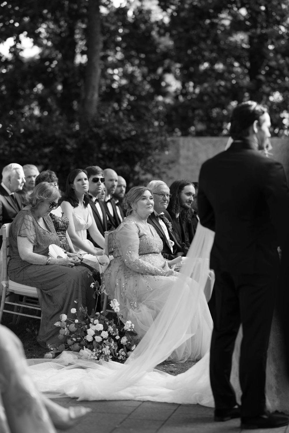 Wedding ceremony guests seated outdoors at a formal garden celebration in black and white photography.