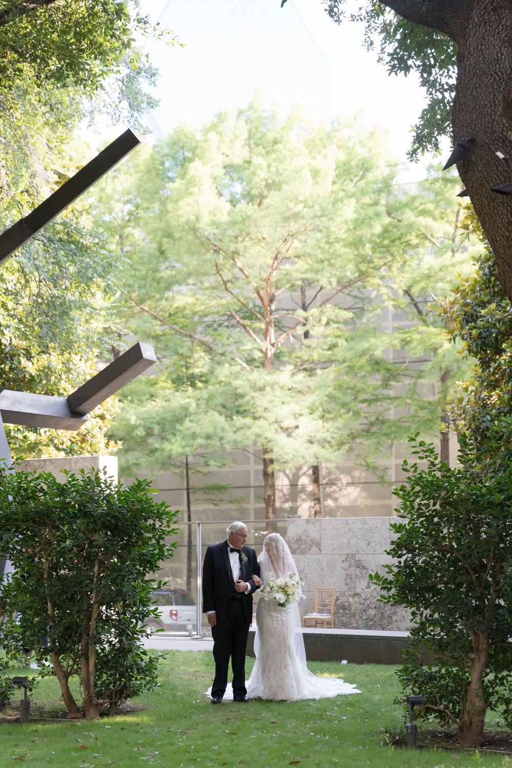 A scenic garden wedding ceremony takes place outdoors among lush greenery and trees in natural daylight.