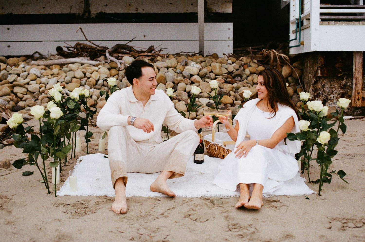 Film photo of couple sitting on blanket, enjoying champagne.