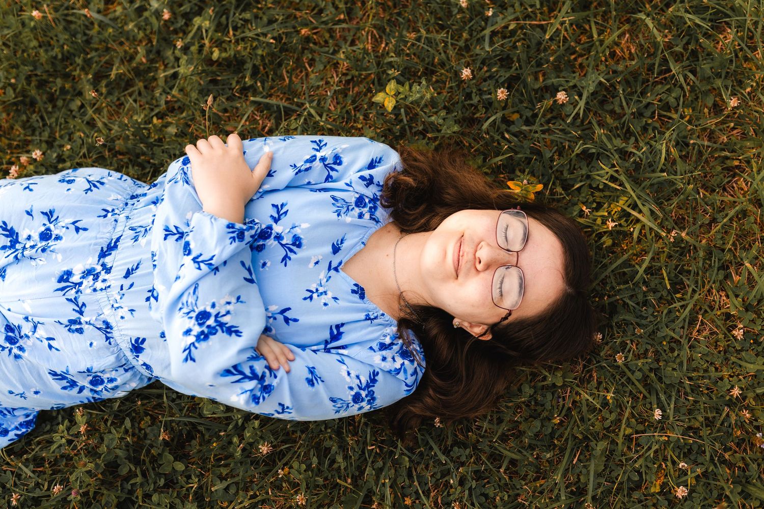 Person wearing blue and white floral dress lying on grass with closed eyes in peaceful repose.