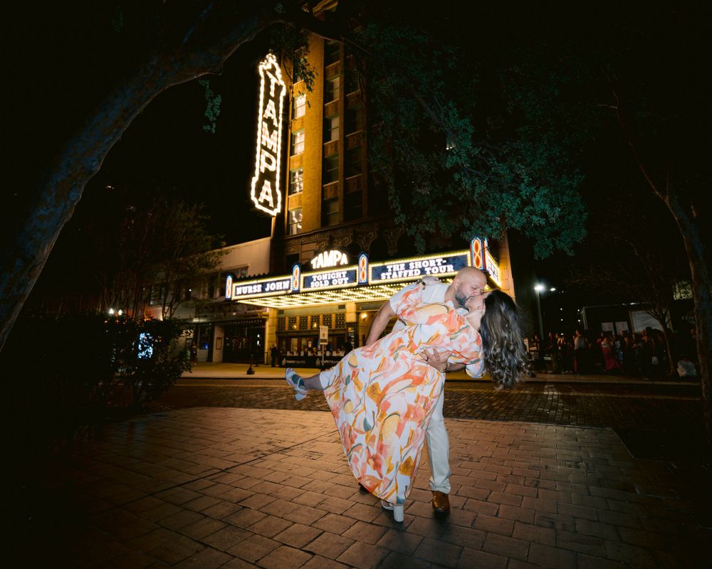 A couple in traditional Japanese kimono dances at night in front of an illuminated theater marquee.