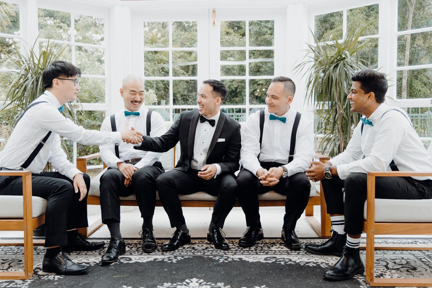 A group of groomsmen in black and white formal attire sit together captured by Apertured Media Auckland Wedding Photographer.