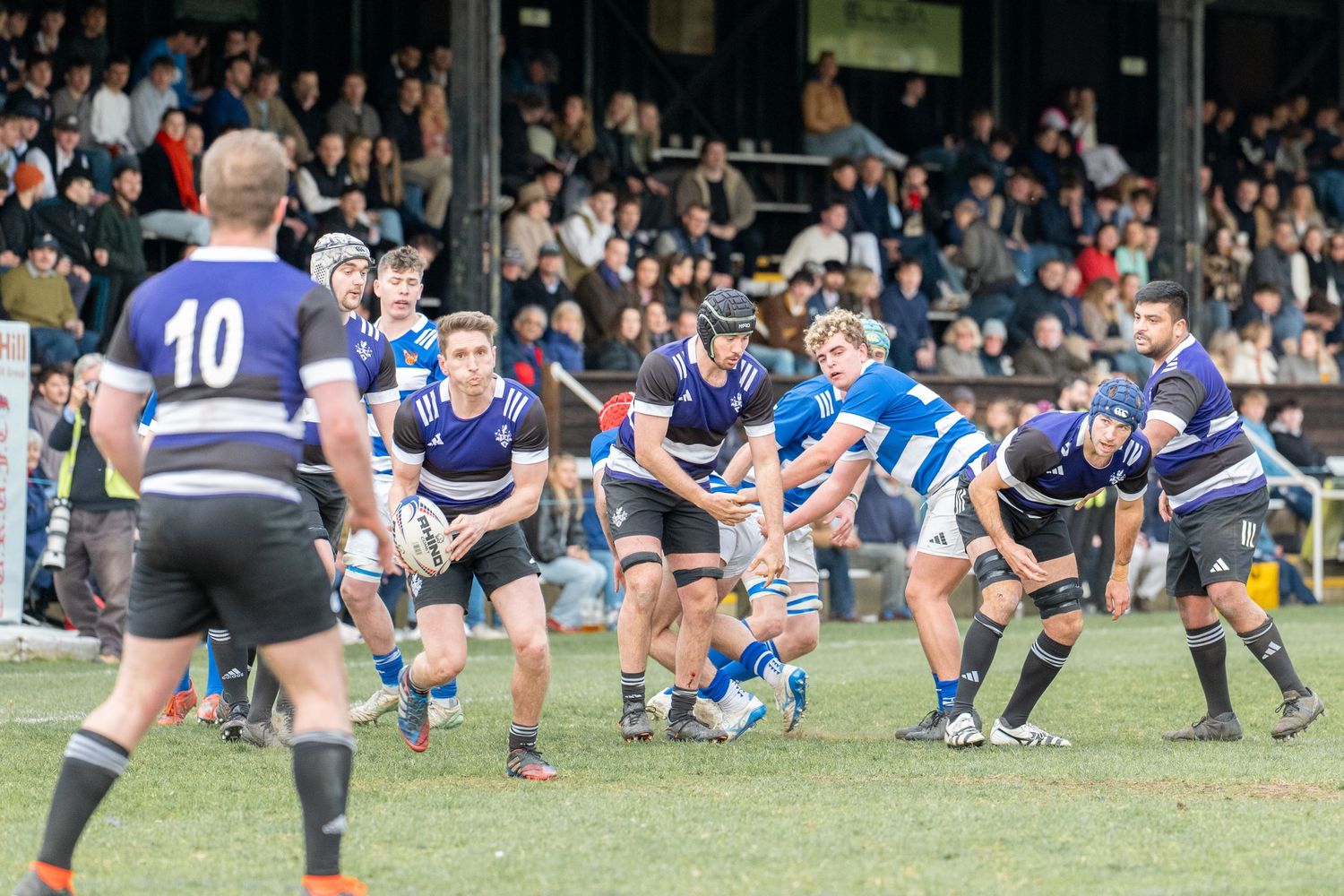 Rugby players locked in a scrum formation during an intense match with spectators watching from the sidelines.