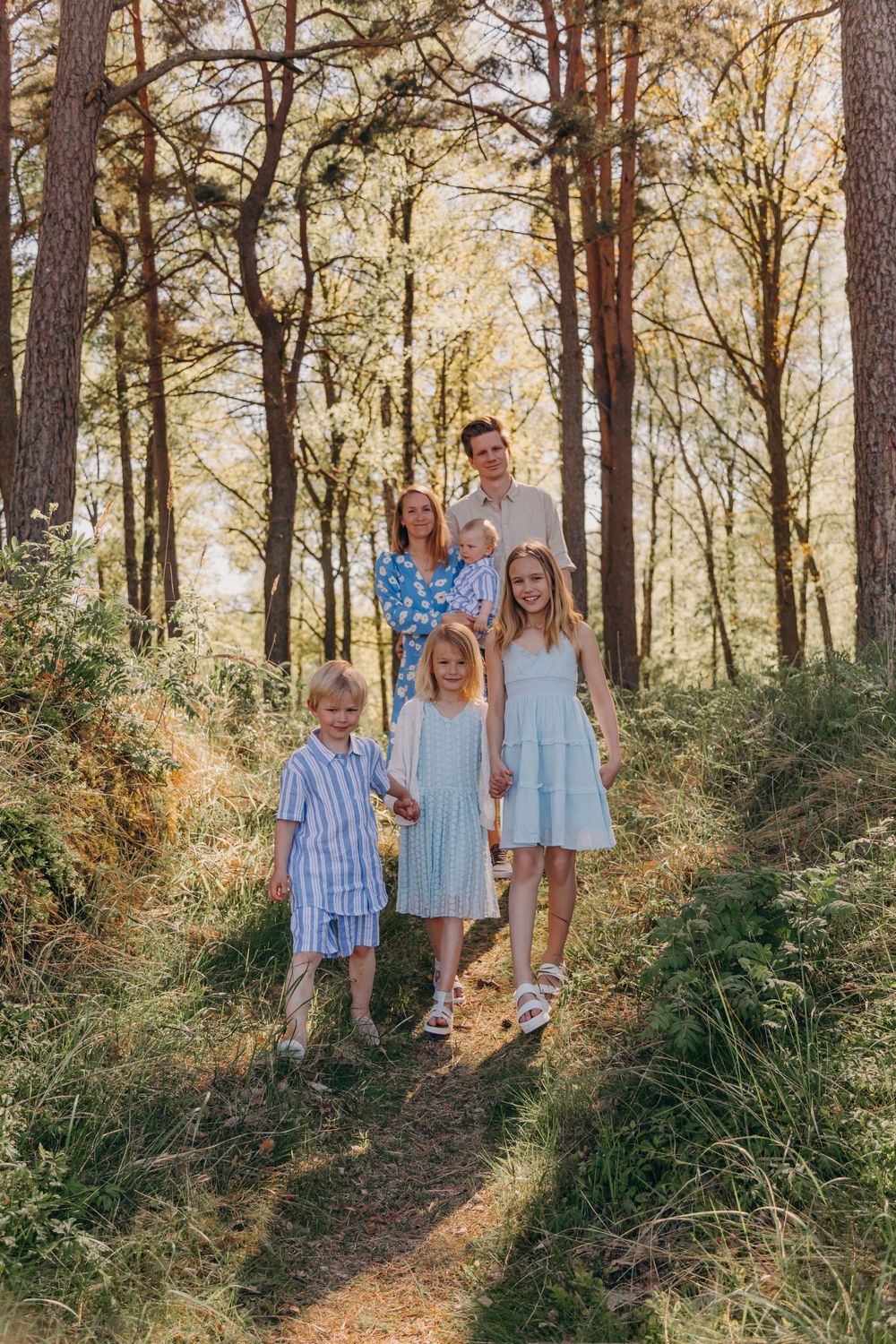 Family of five posed together on forest trail during golden hour.