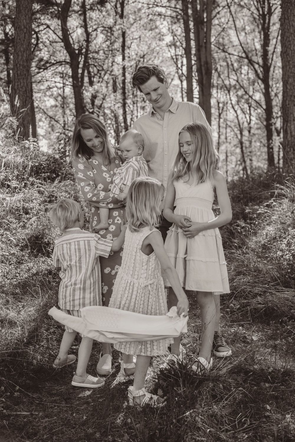 A black and white portrait of a family group standing together in a wooded forest setting.