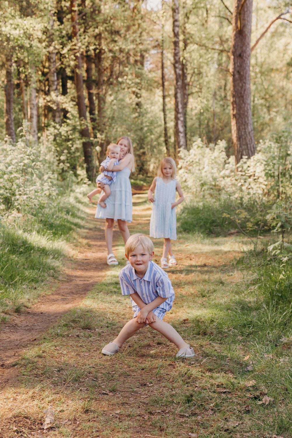 Children in light summer clothing playing and laughing on a sunlit forest path.