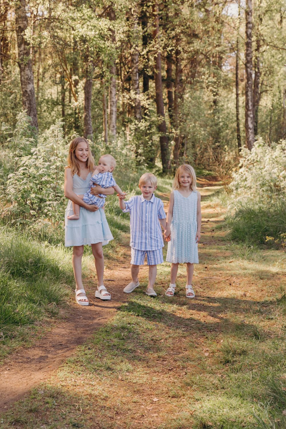 A family walking together on a sunlit forest path lined with tall pine trees on a summer day.