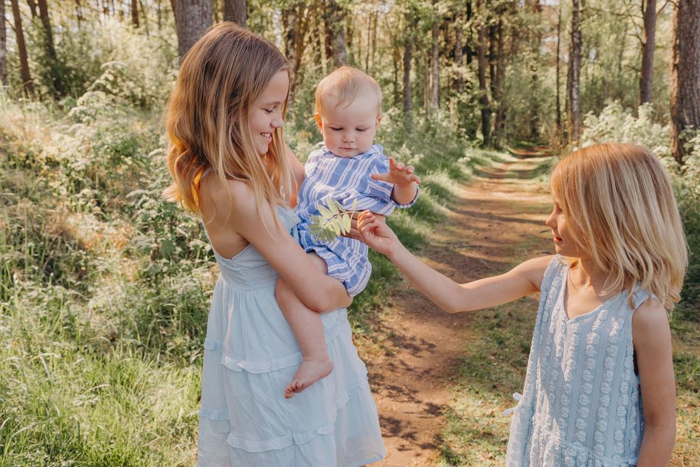 Three people in light summer dresses interacting on woodland trail.