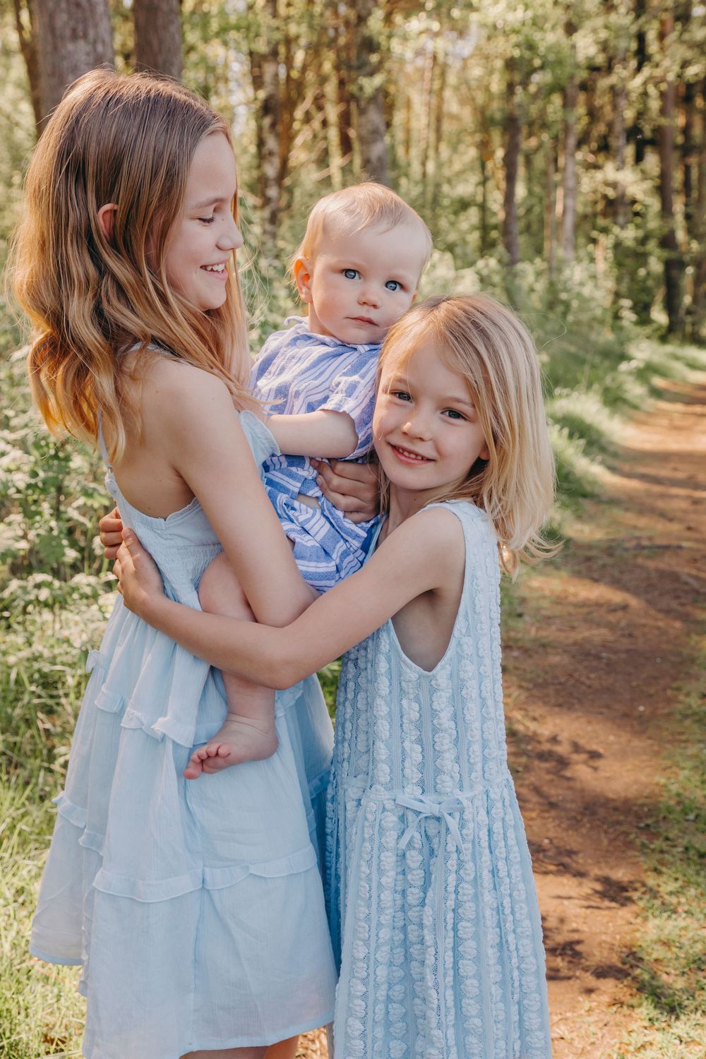 Three siblings in matching light blue outfits share a joyful moment together on a wooded forest trail.