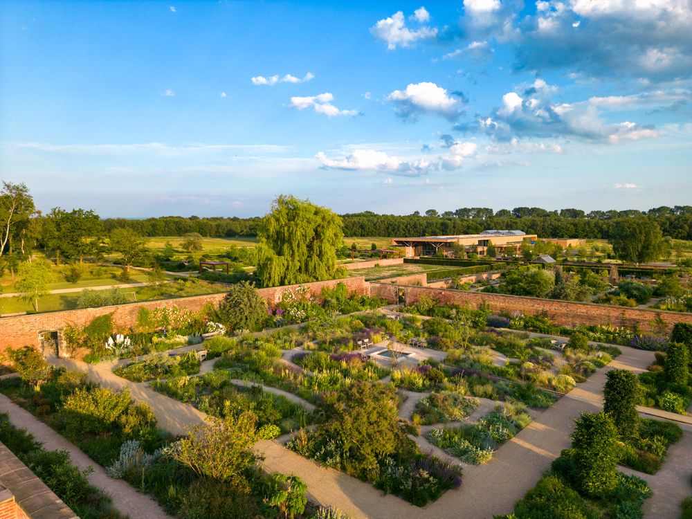 Aerial view of a formal garden with neat pathways and planted beds under a bright blue sky with puffy clouds.