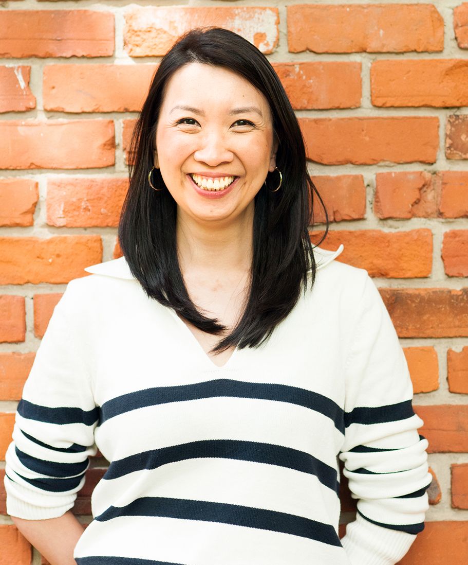 Person wearing a black and white striped sweater smiles warmly against a brick wall backdrop.