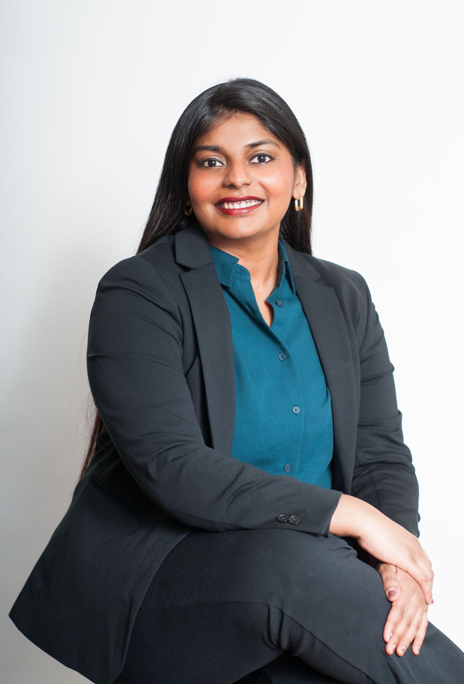 Professional headshot portrait of person in dark blazer and teal blouse against white background.