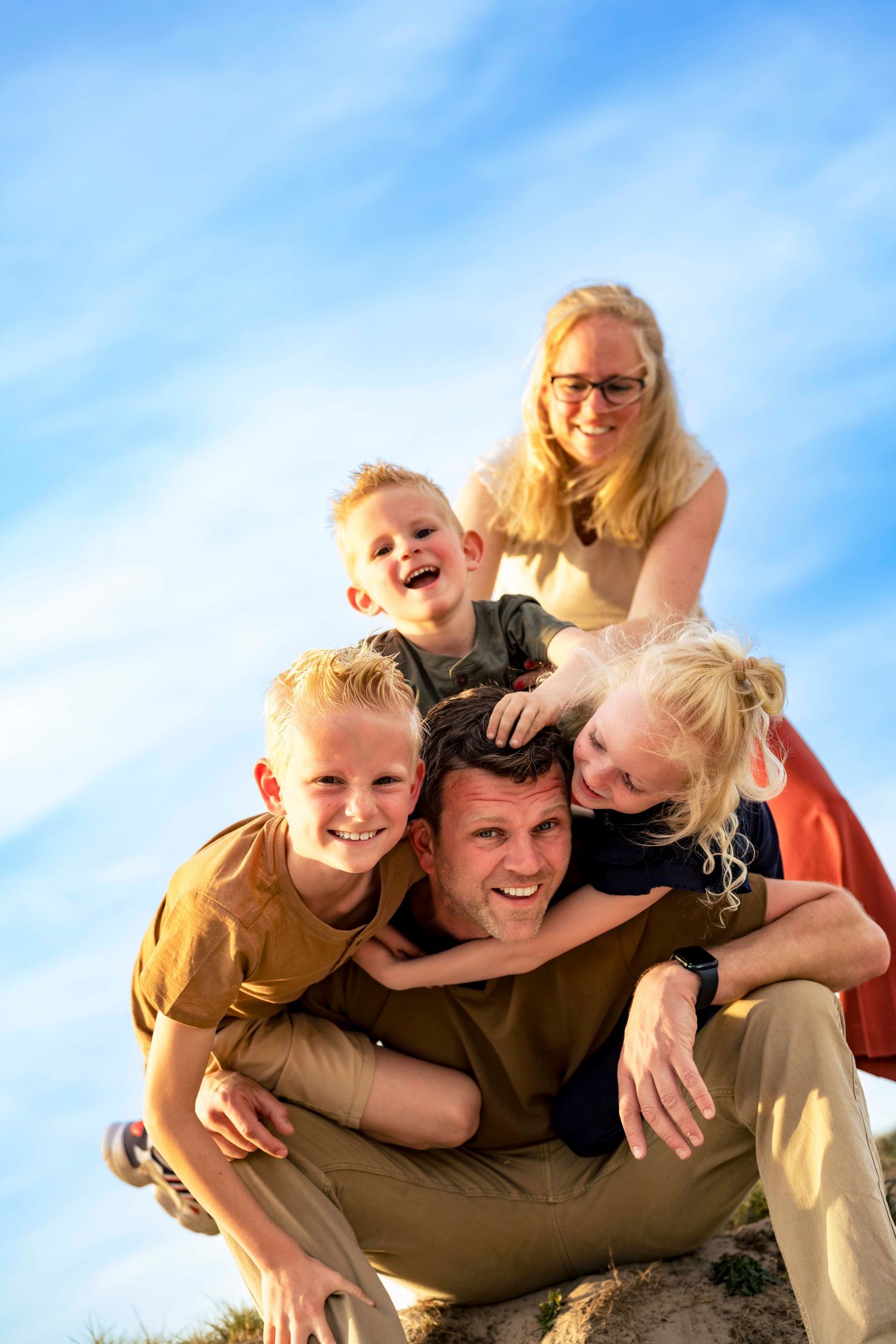 Family enjoying a playful moment together against a bright blue sky during an outdoor photo session.