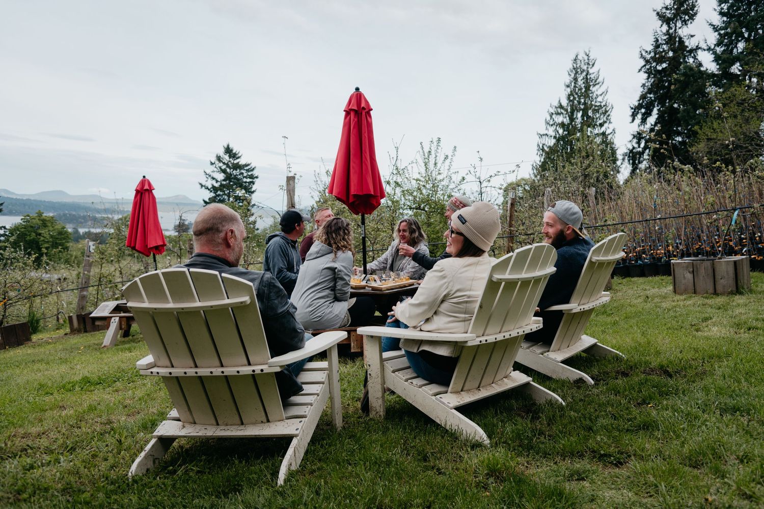 Ciderworks picnic table with red umbrella and a group of visitors enjoying cider on salt spring island
