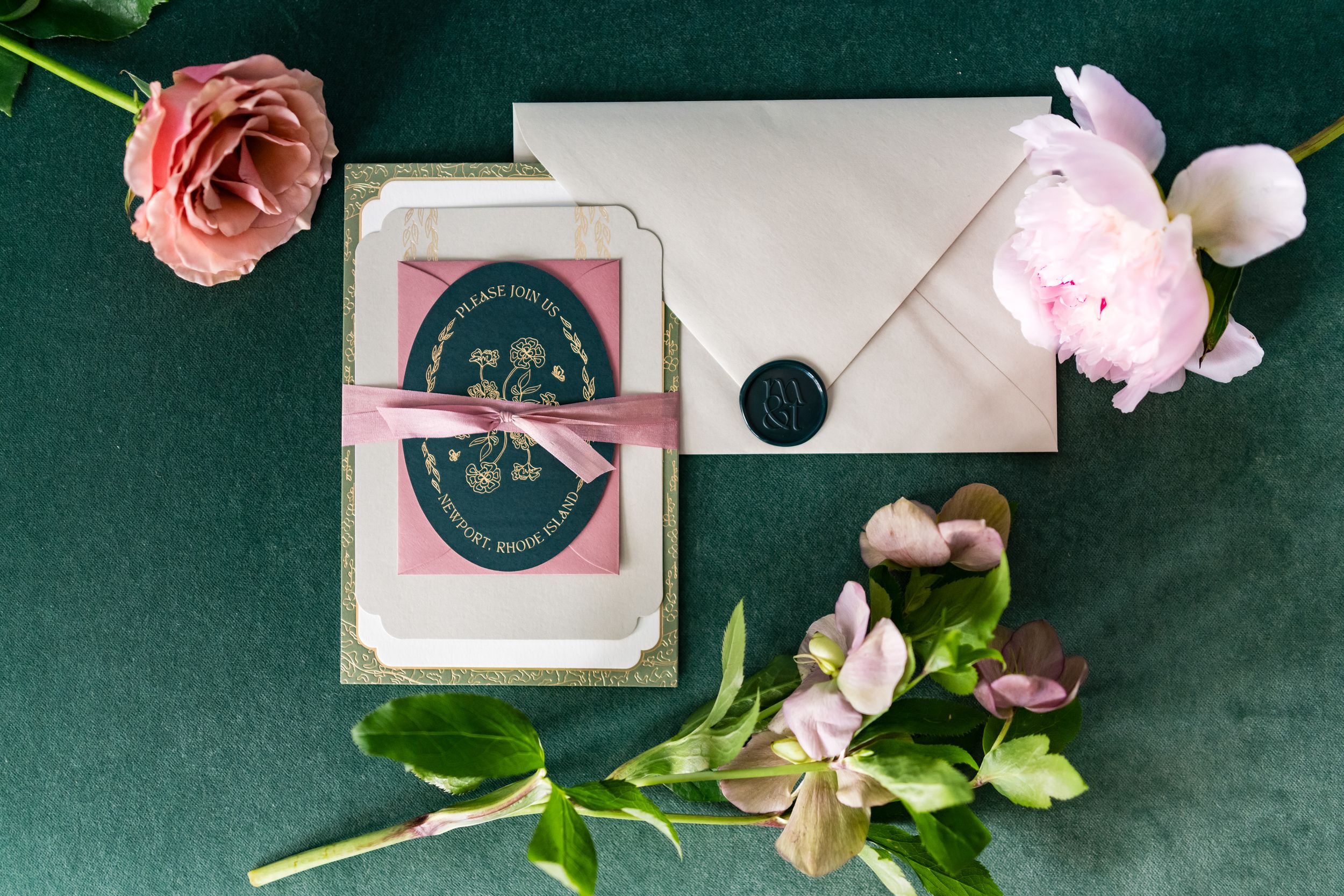 Pink roses and floral arrangements lay scattered on a dark green surface alongside elegant white stationery and paper items.
