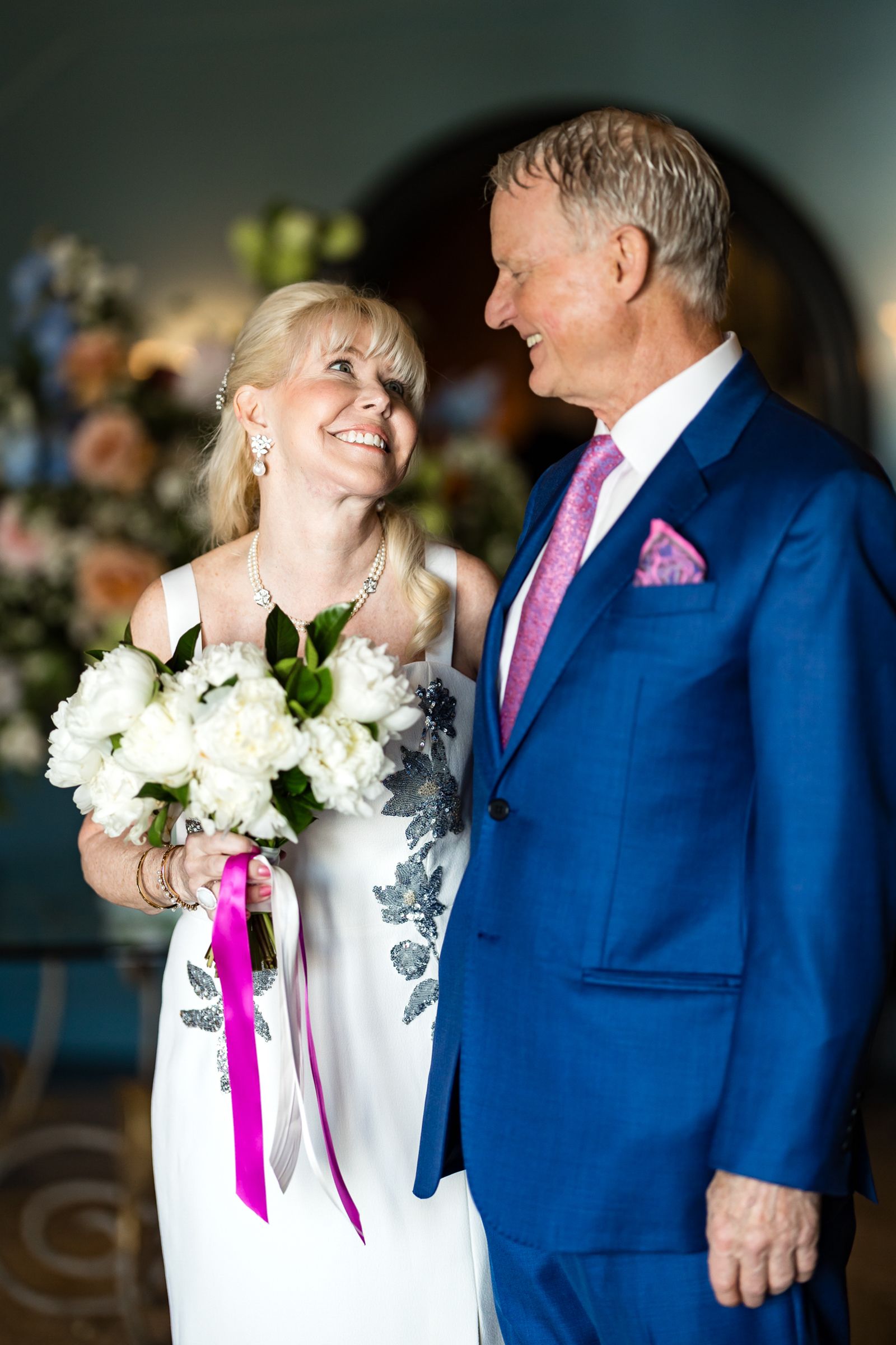 A couple in formal attire share candid intimate moments, with the woman wearing white and man in a blue suit and pink tie.