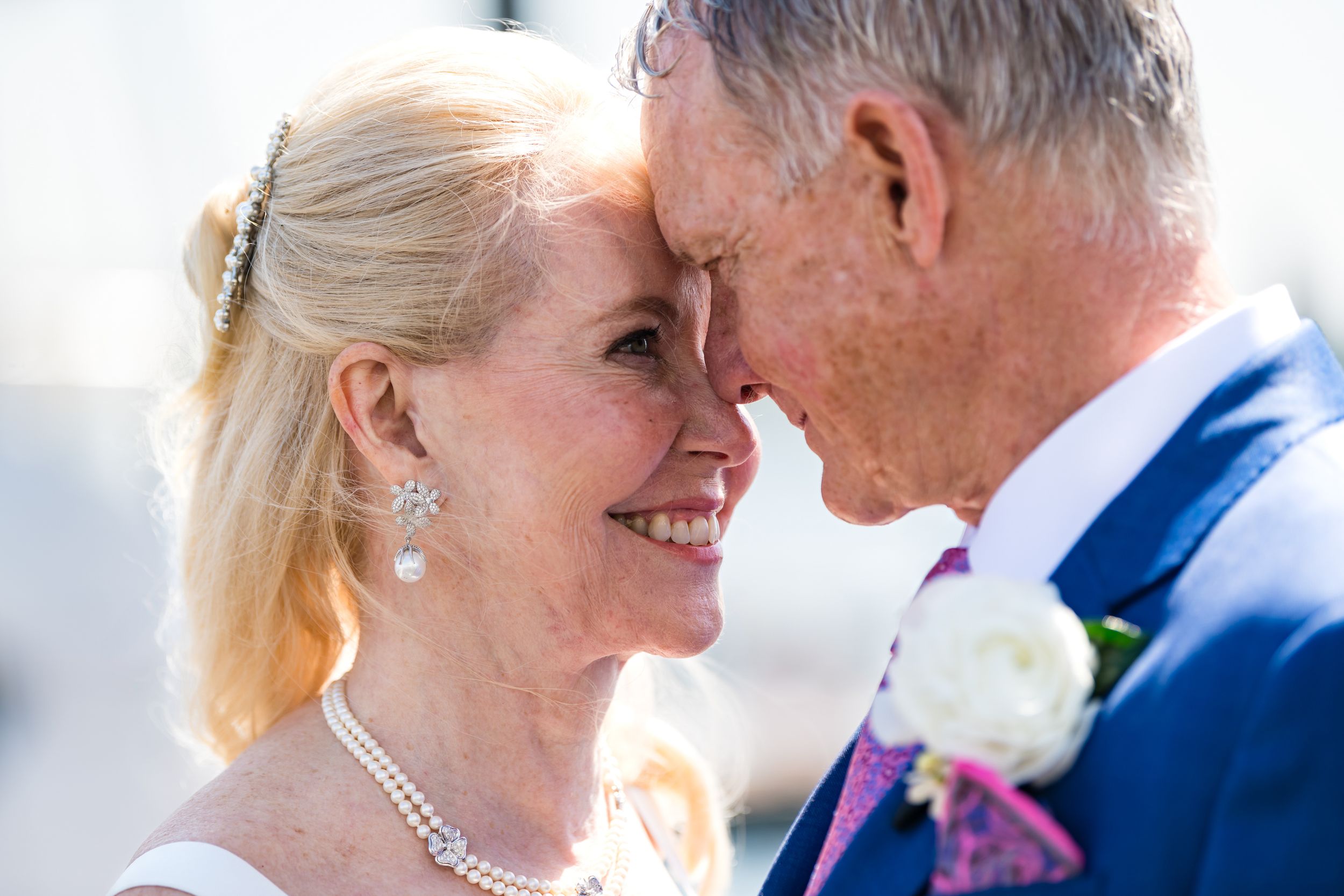 A tender moment between a bride in pearls and her companion during a wedding ceremony outdoors.