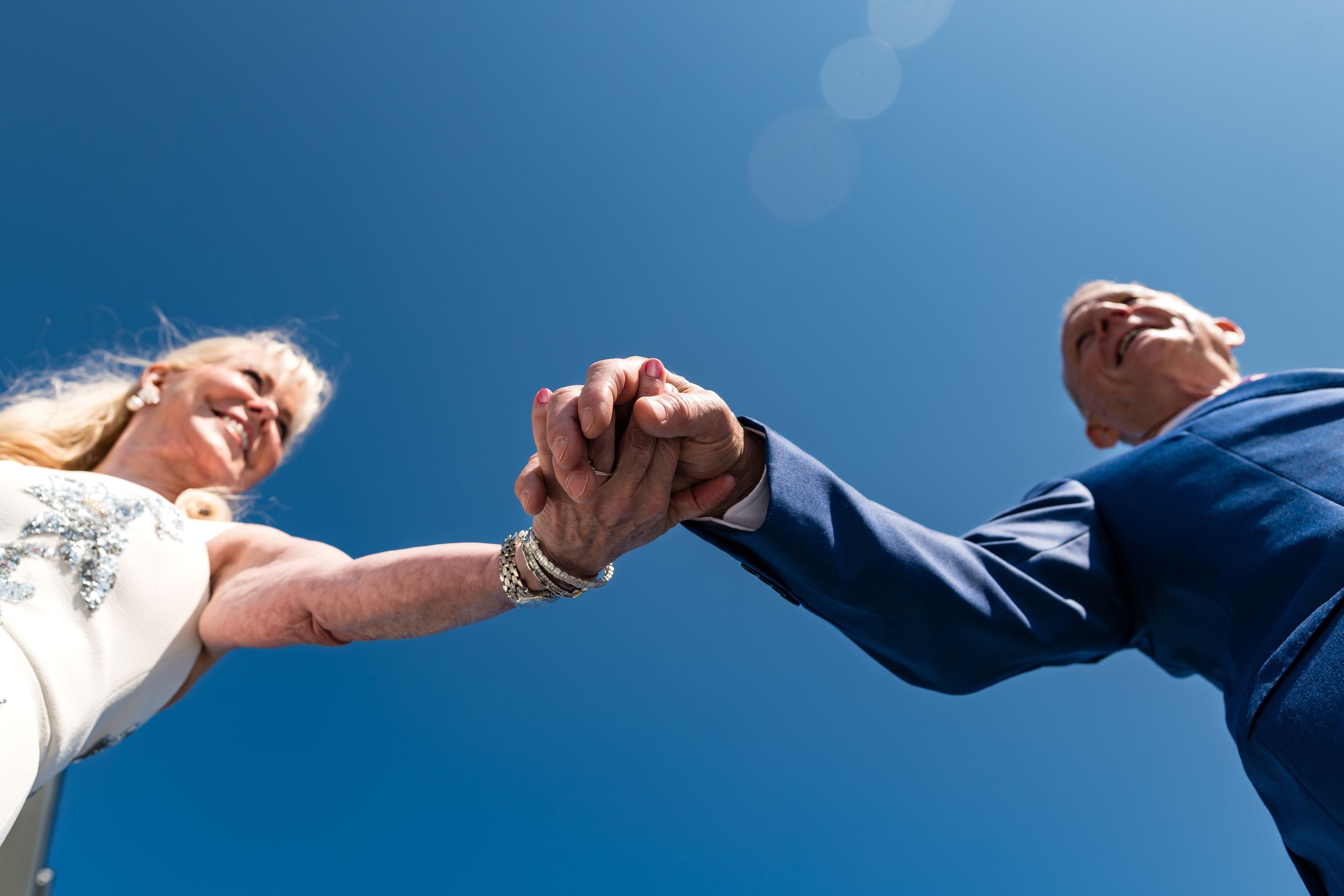 Low angle view of two people holding hands against bright blue sky background.