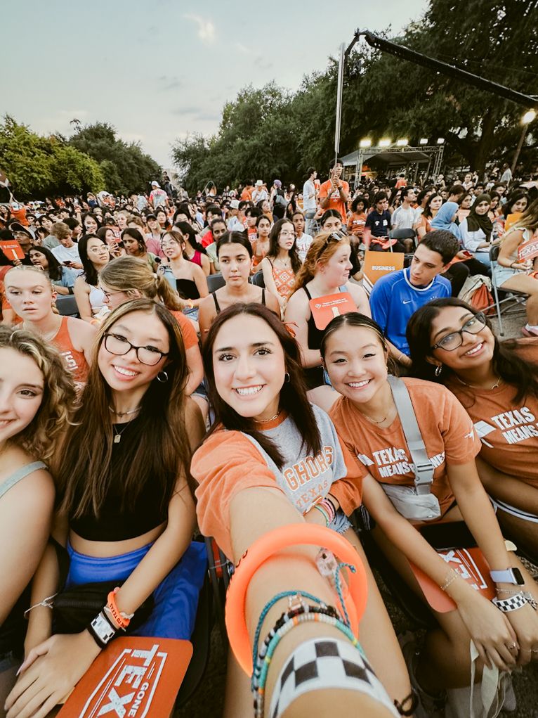 Large crowd of students in orange shirts gathered outdoors at a university event with string lights overhead.