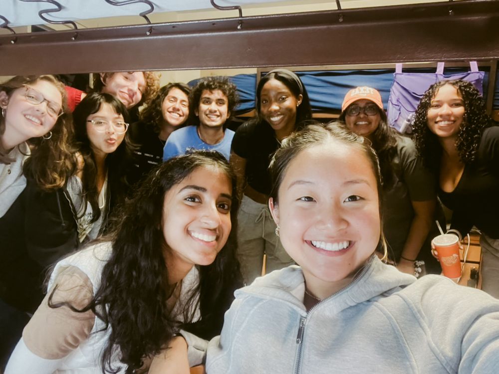 A diverse group of people smiling together in a casual indoor setting taking a selfie photo.