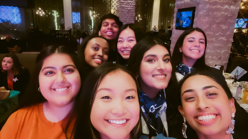 A group of smiling friends taking a close-up selfie together at a restaurant.