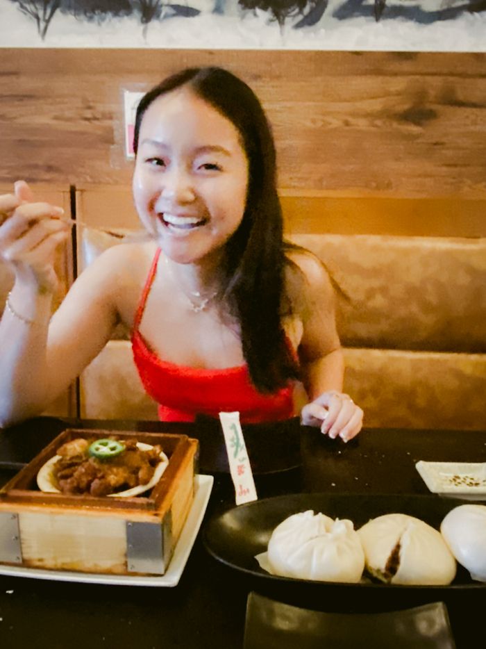 A diner smiles while seated at a restaurant table with steamed buns and other Asian dishes.