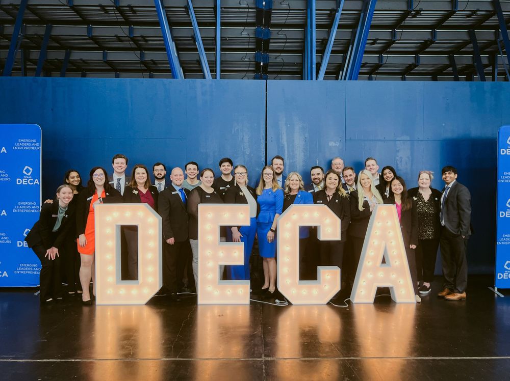 A group stands behind large illuminated DECA letters during what appears to be a conference or event.