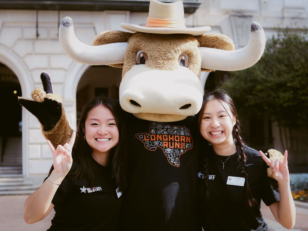 University mascot in a large longhorn costume and white cowboy hat poses with two staff members making hook 'em horns signs.