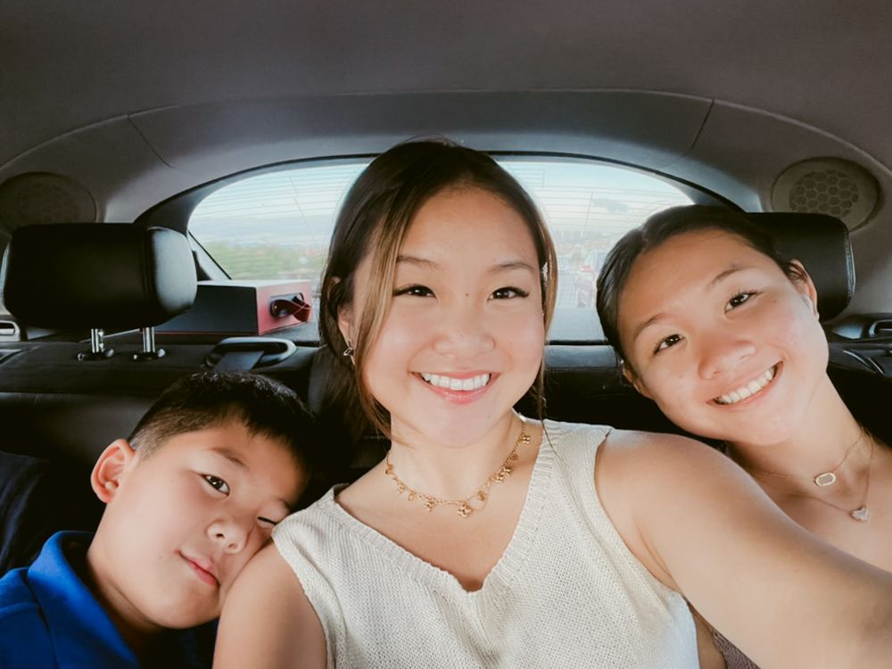 Three people taking a selfie together from inside a car with dark interior.