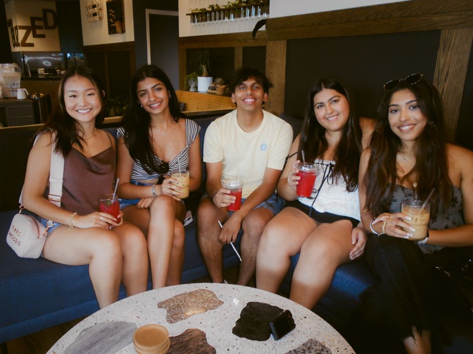 Friends gather around a coffee table enjoying drinks and snacks in a cozy indoor setting.