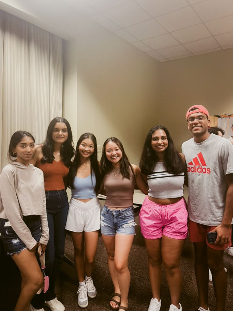 A group of young friends in casual summer outfits pose together in an indoor setting.
