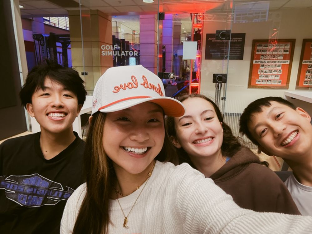 A group of friends pose together for a close-up selfie in an indoor setting with purple lighting.