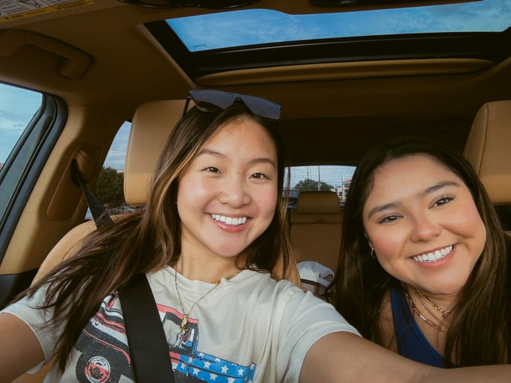 Two passengers taking a selfie while sitting in a car with a sunroof visible above.