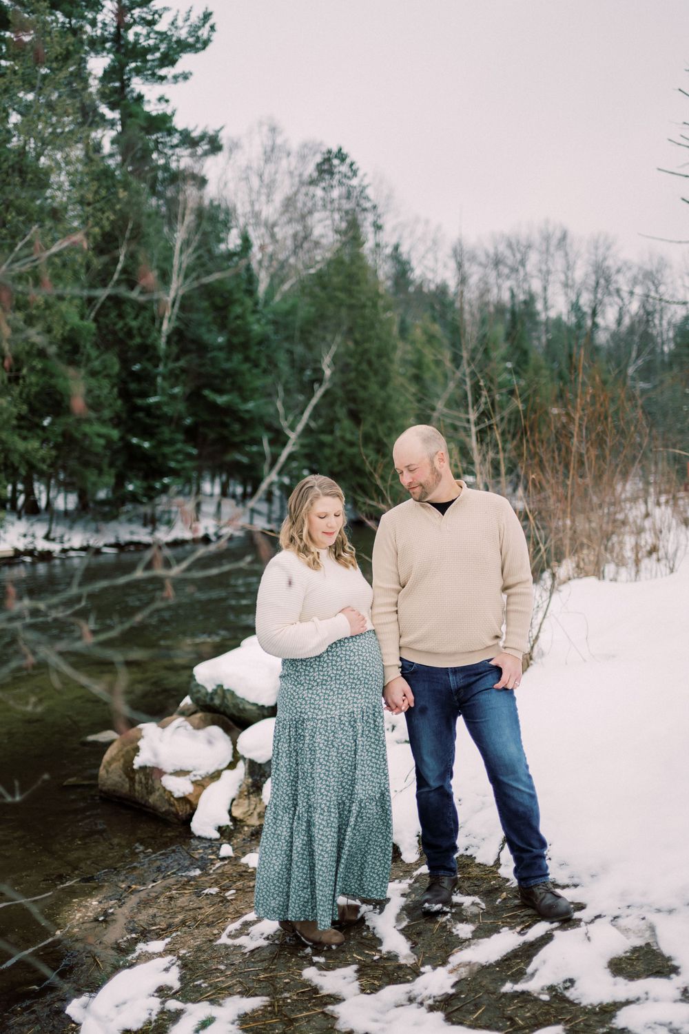 A couple sharing an intimate moment by a snowy riverbank in winter.