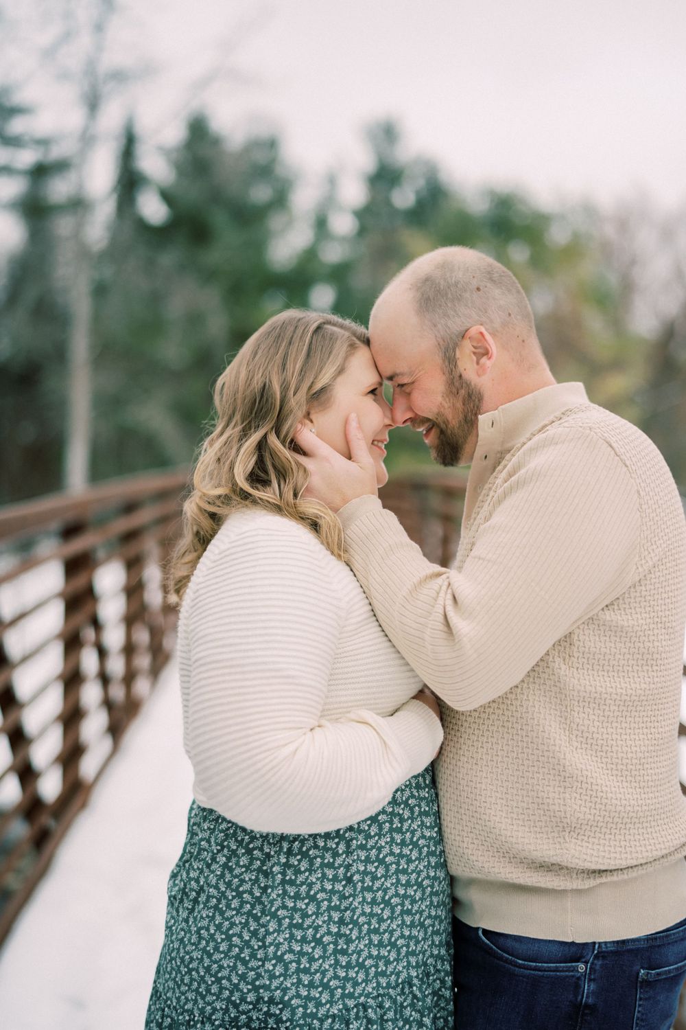 Intimate winter portrait of couple sharing tender moment on snowy bridge.