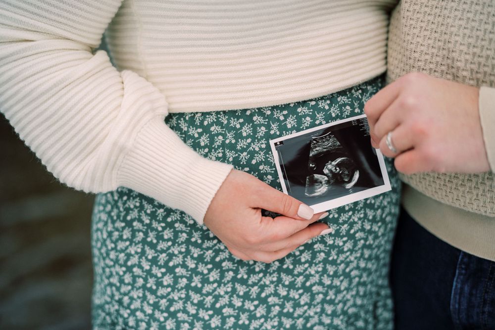 Close-up of hands holding ultrasound photo against floral dress during pregnancy announcement.