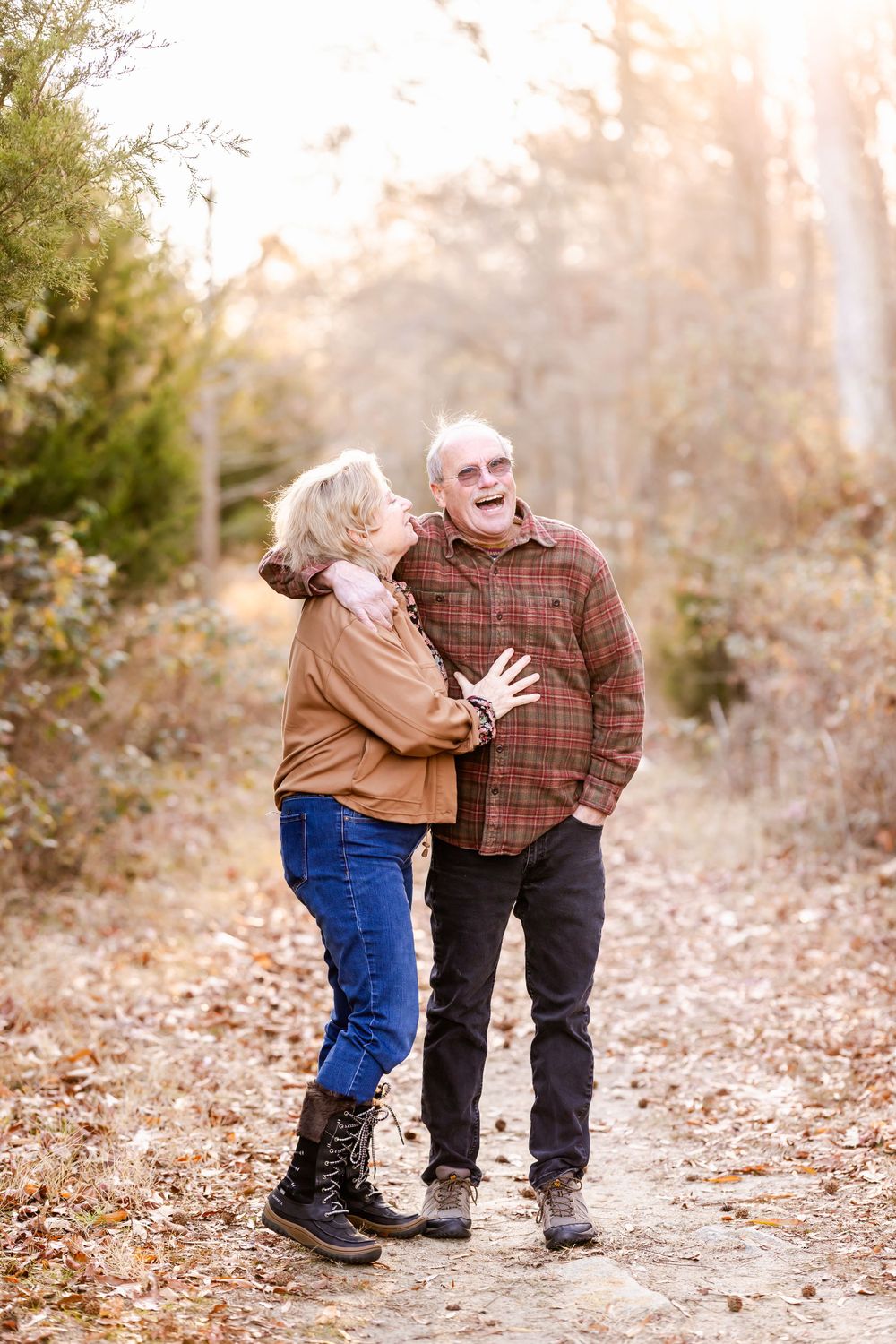 A couple shares a joyful moment while walking on a leaf-covered autumn trail.