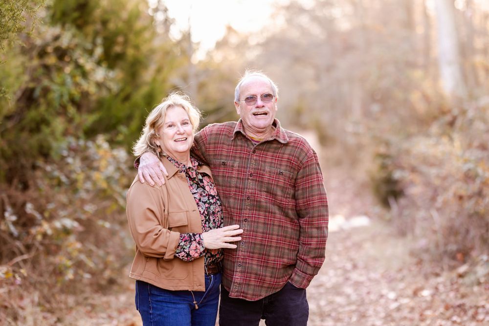 A couple stands together on a wooded path during autumn.